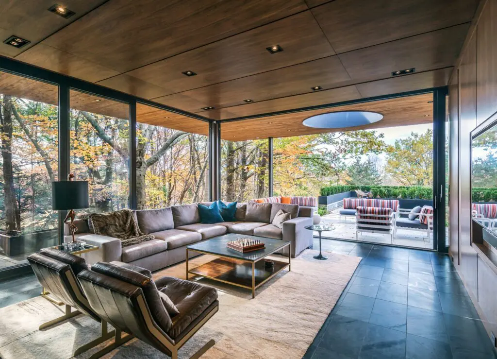 Modern living room with floor-to-ceiling glass and forest views.