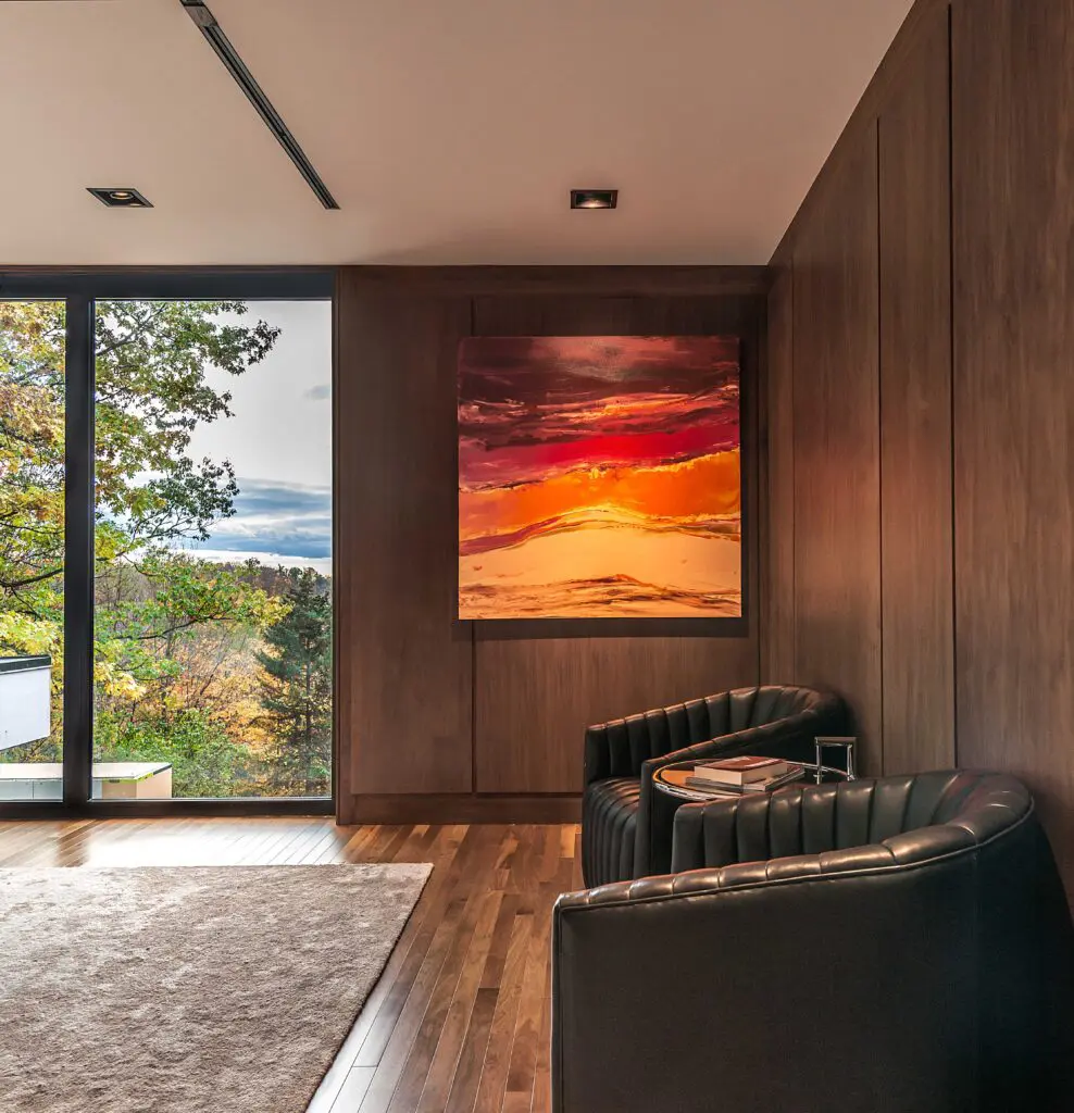 Modern sitting area with walnut wall paneling, leather lounge chairs, and large landscape artwork.