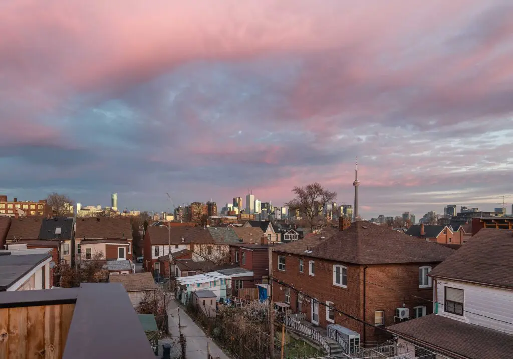 Elevated view over residential rooftops toward downtown Toronto skyline and CN Tower at dusk.