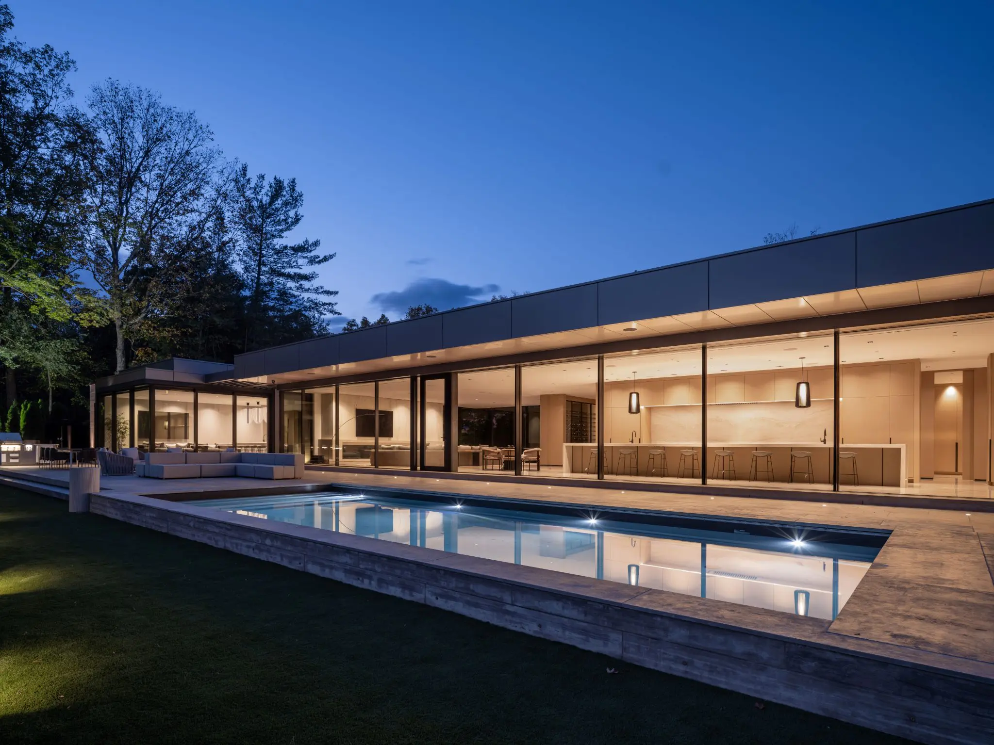 Modern home exterior with pool and glass façade illuminated at twilight.