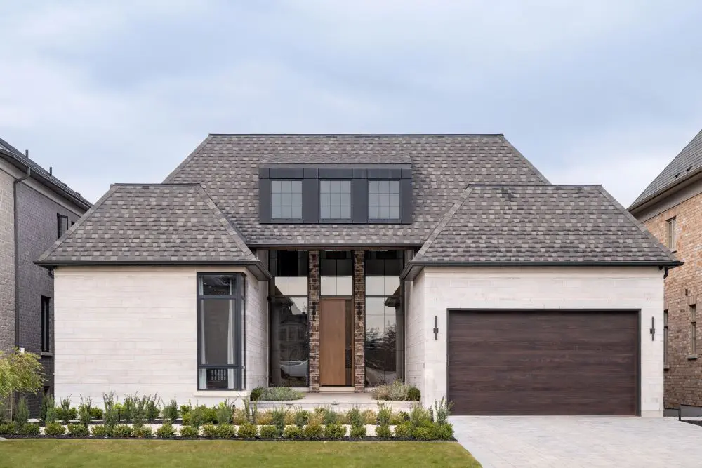 Front view of modern residence with gabled roof, large windows, and elegant stone detailing.