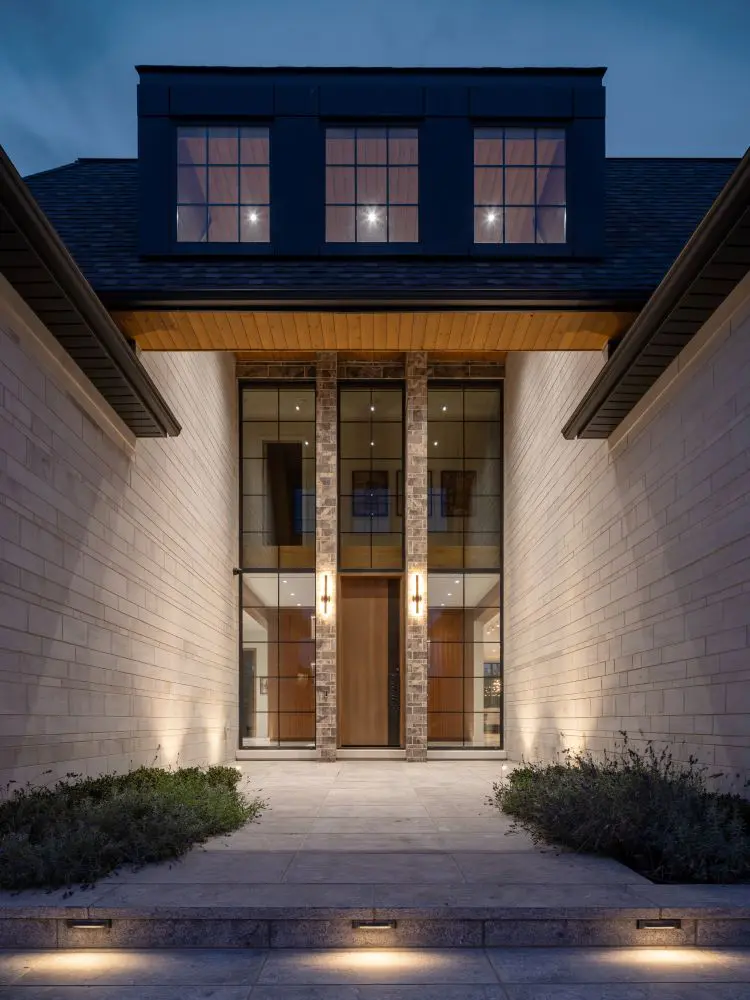 Grand entryway with tall glass panels and wood door framed by stone columns.