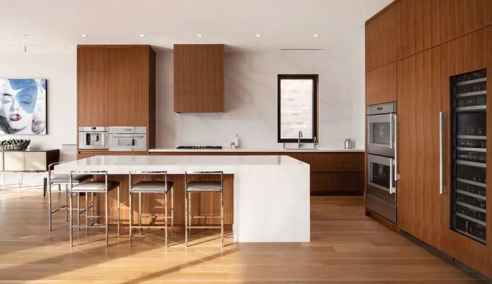Modern kitchen with walnut cabinetry, white island, and built-in stainless-steel appliances.
