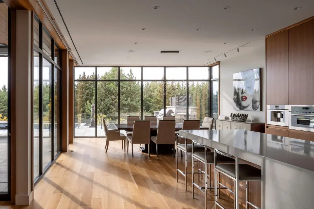 Open dining and kitchen area with floor-to-ceiling windows overlooking a forested view.