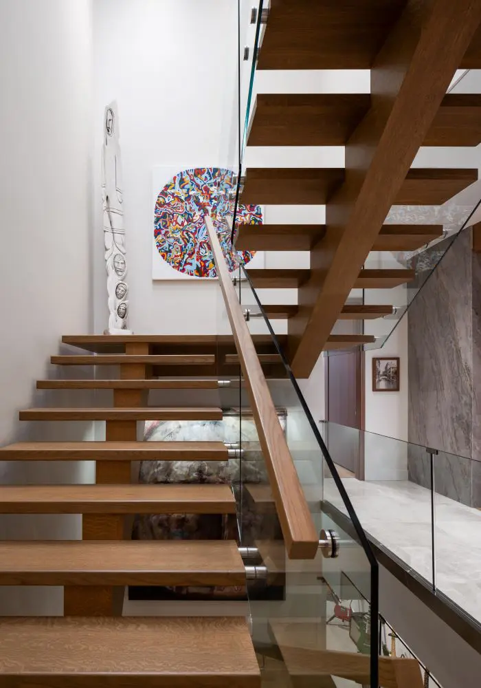Floating wood staircase with glass railing and contemporary art display.
