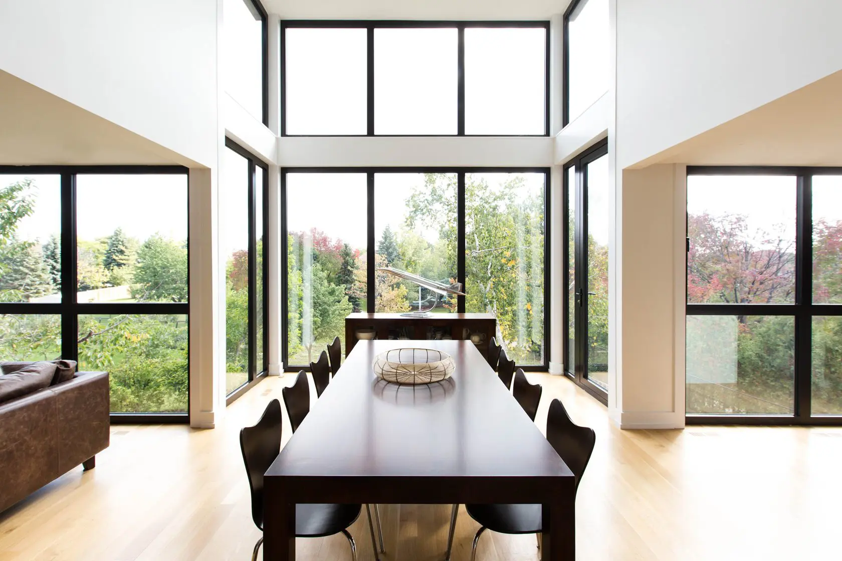 Dining area with tall windows overlooking lush greenery.