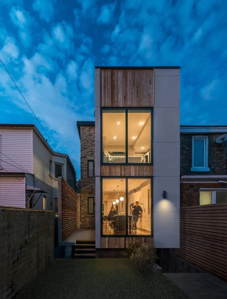 Rear exterior view of modern home with large glass windows and wood panel accents at dusk.