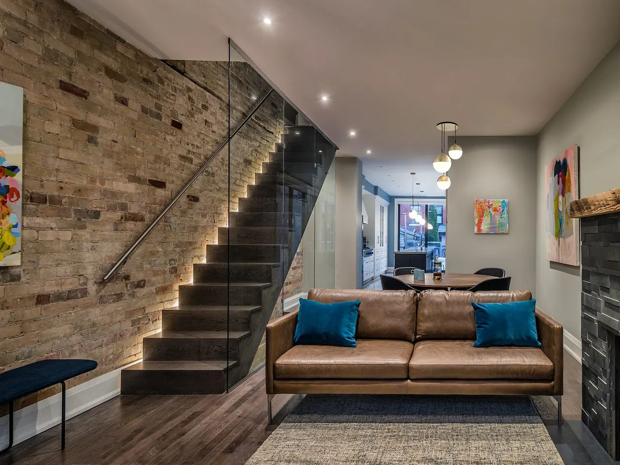 Open-concept living space with illuminated staircase and modern leather sofa.