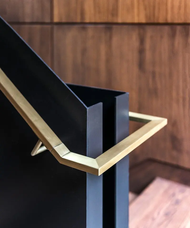 Detail of modern staircase with brass handrail and black steel finish.