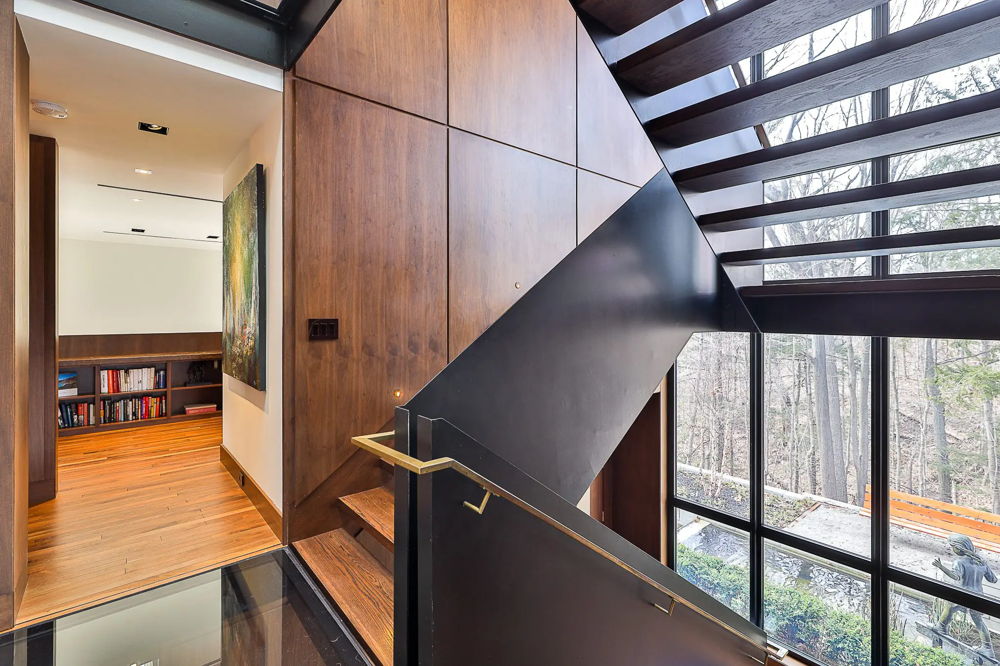 Wood and steel staircase beside large windows overlooking trees.