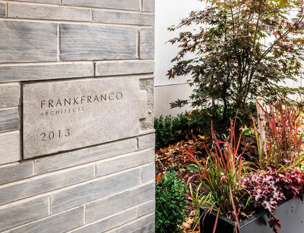 Architectural stone plaque on modern brick wall beside landscaped garden.