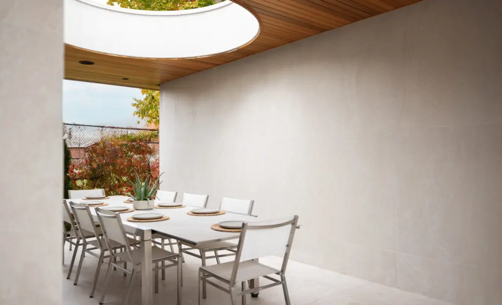 Covered outdoor dining area beneath circular oculus with porcelain walls and modern landscape backdrop.