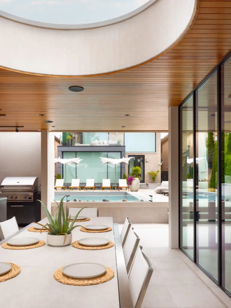 Outdoor dining area with cedar ceiling and oculus connecting to pool and modern residential landscape.
