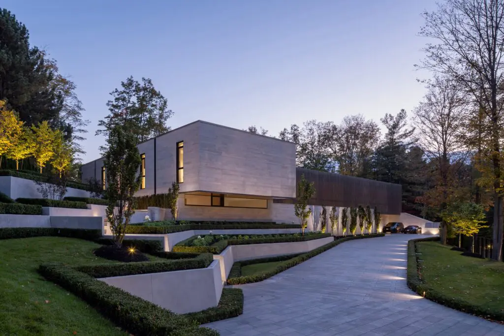 Modern hillside home with terraced landscaping and illuminated driveway.