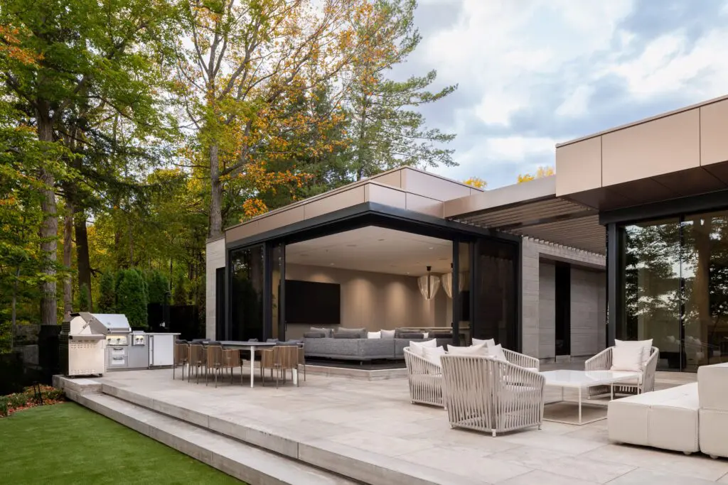 Outdoor terrace with dining area, lounge seating, and open indoor–outdoor living framed by forest views.