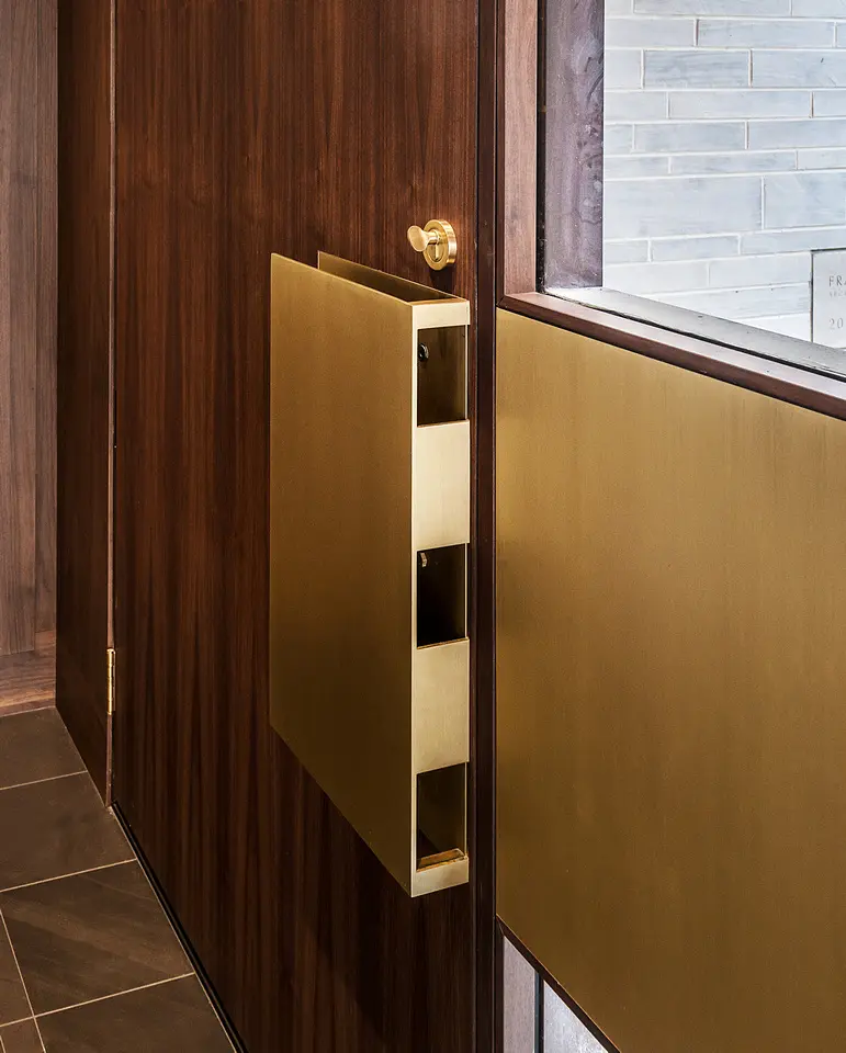 Close-up of custom brass door pull on dark wood interior door with minimalist detailing.
