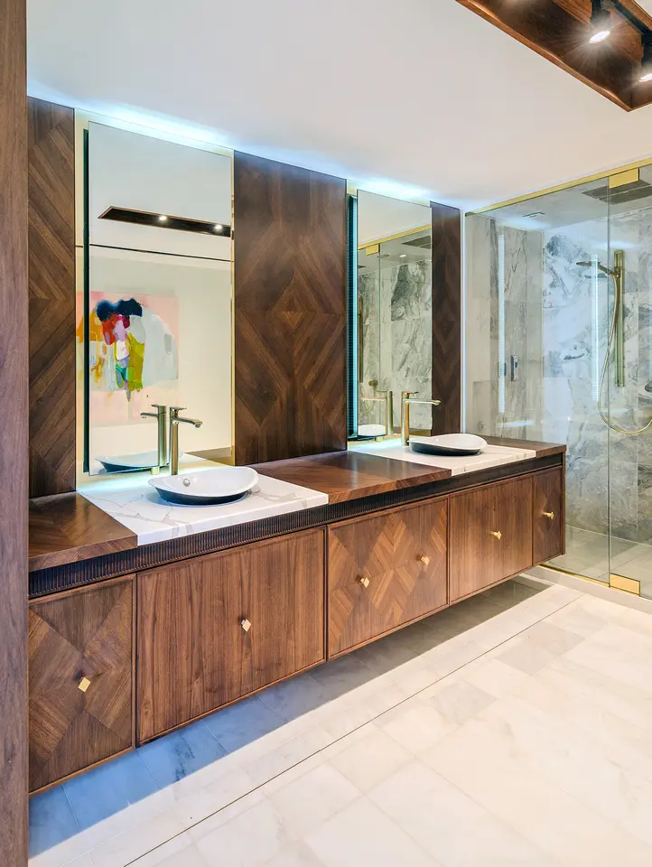 Luxury ensuite bathroom with double vanity, brass fixtures, wood cabinetry, and marble shower.