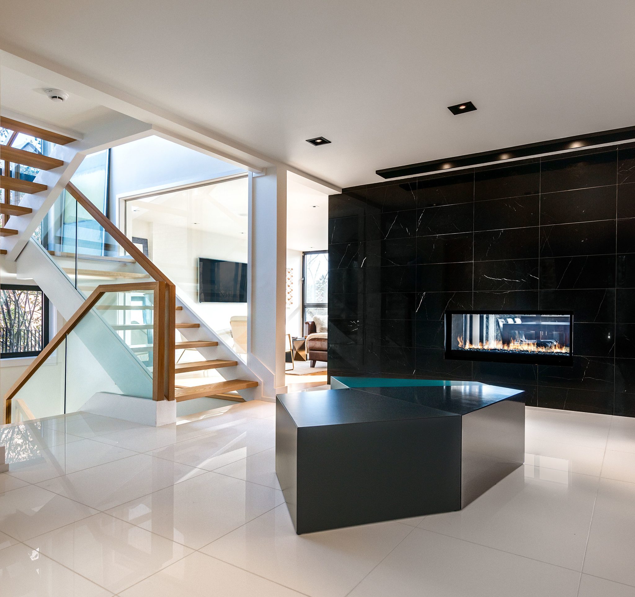 The large entrance foyer of a custom built home with beautiful black marble fireplace and glass staircase designed by FrankFranco Architects on their Deja View Project. Are you building a custom home? Connect with us today.