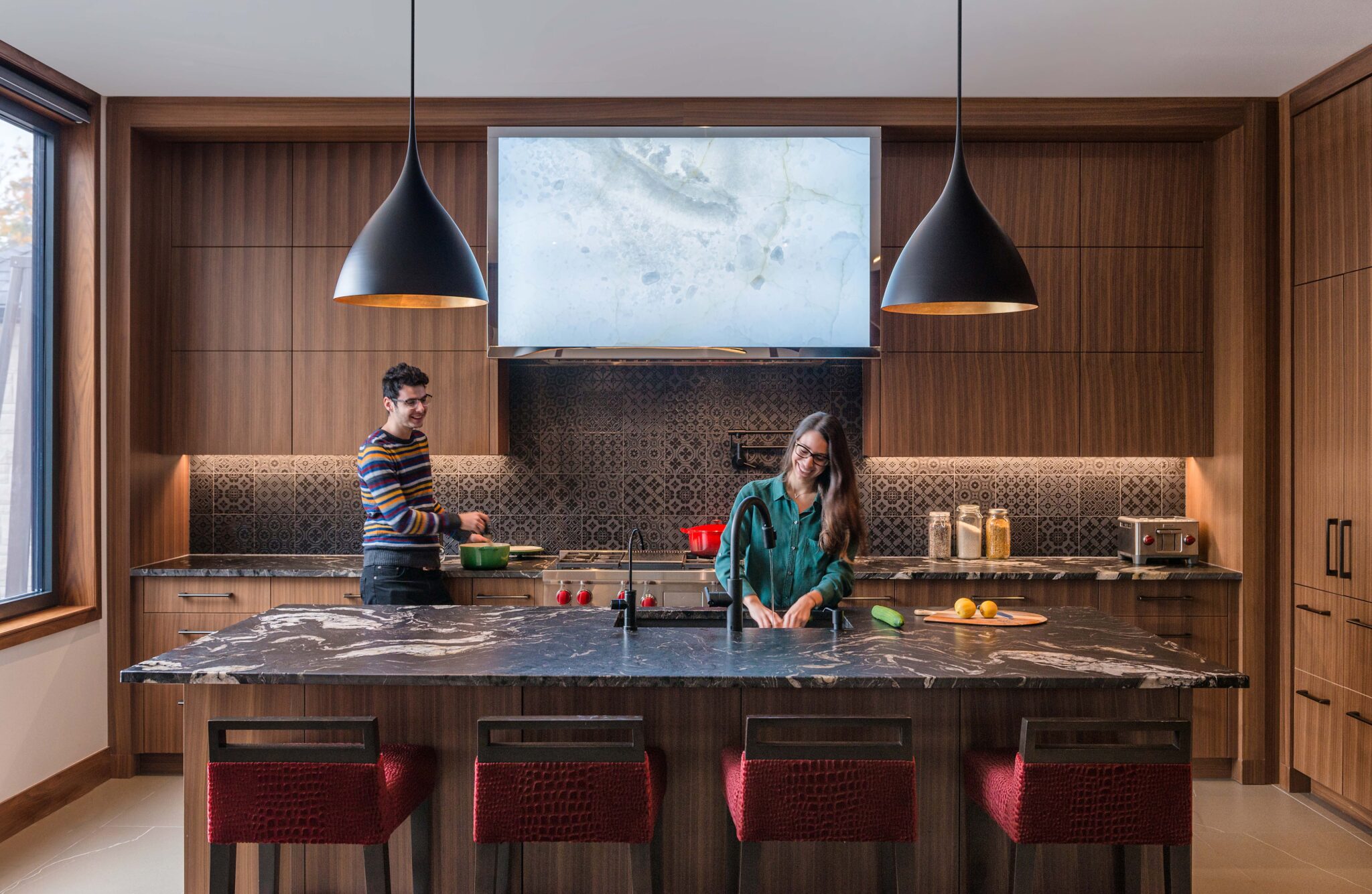 Modern kitchen with wood cabinetry, black marble island, and pendant lighting.
